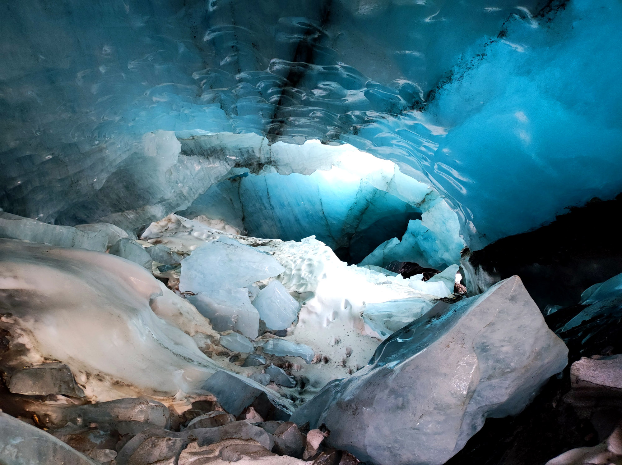 Inside a blue ice cave with sculpted, translucent walls and jagged ice formations, light filtering through the ice