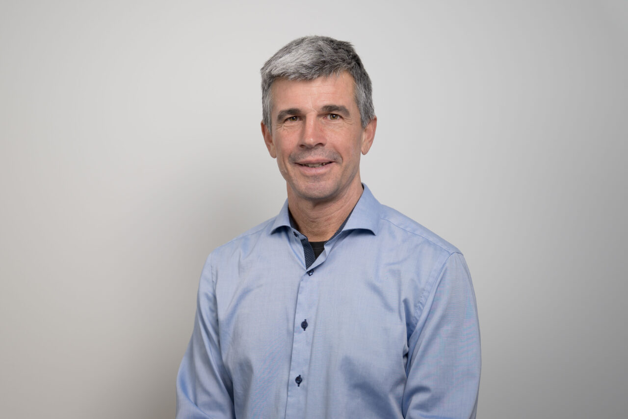 Portrait of a middle-aged man with gray hair wearing a light blue button-down shirt against a neutral gray backdrop.