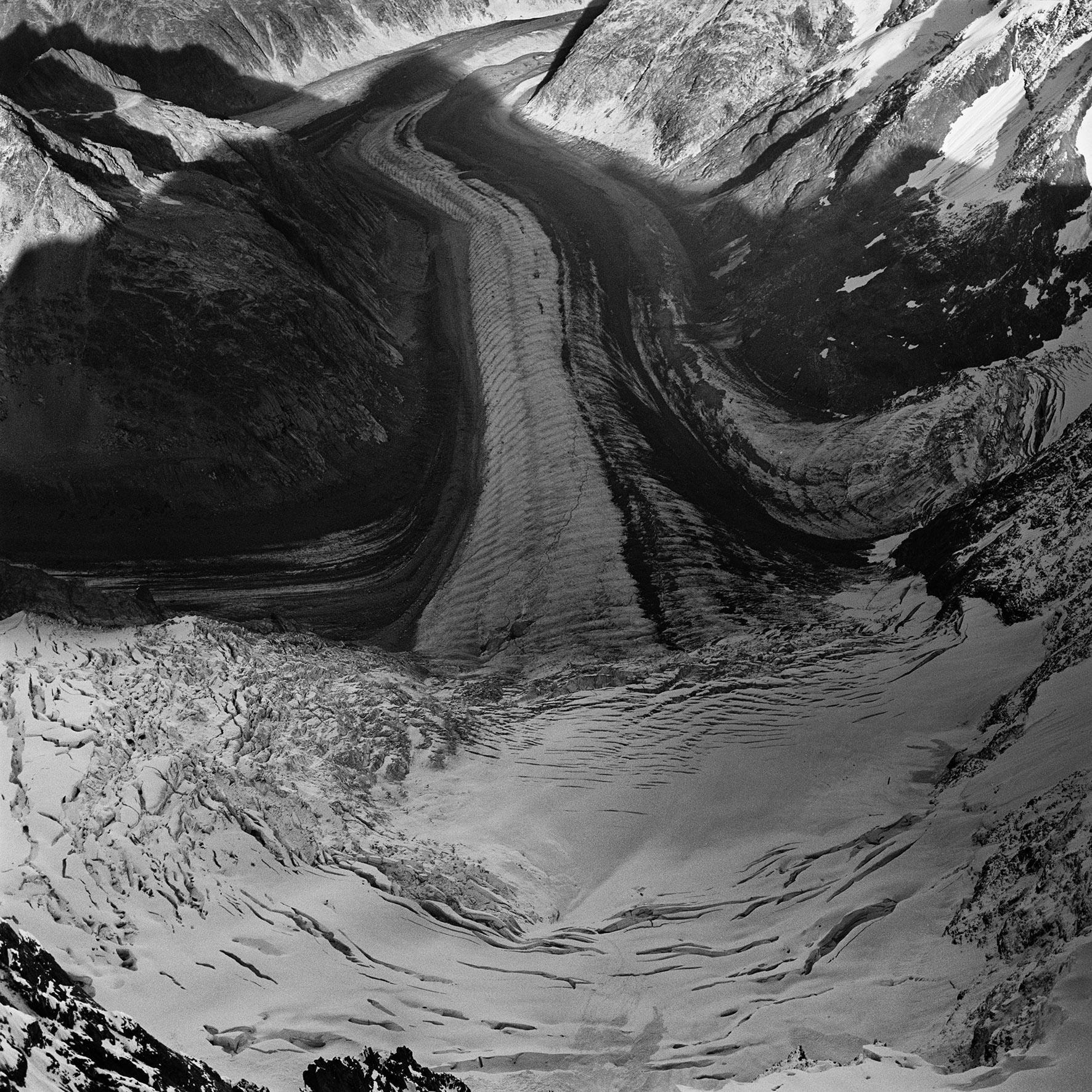 Glacier winding through a rocky mountain valley with snow and crevasses in black and white edge tones.