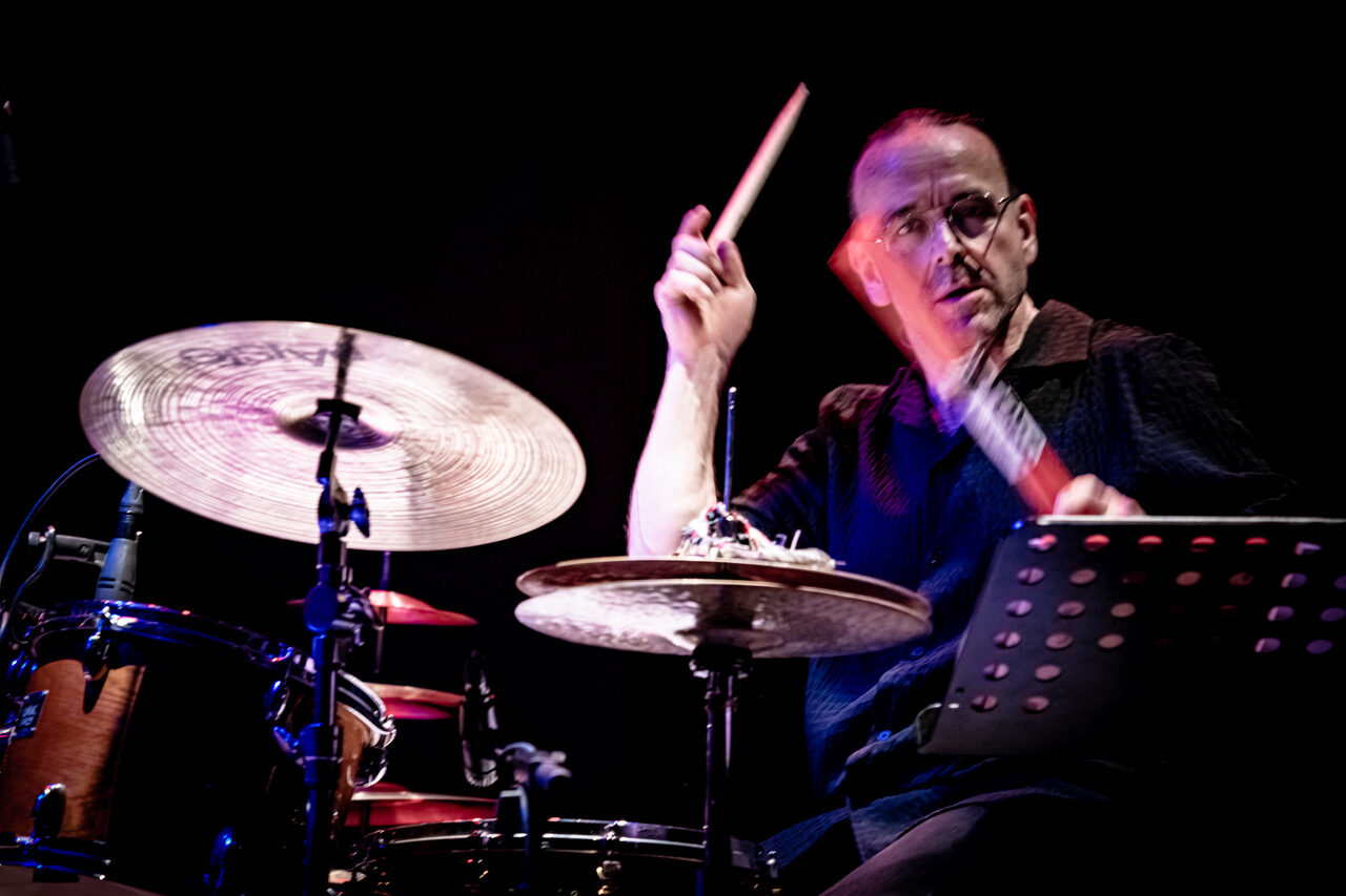 Drummer on stage playing a drum kit, motion blur on his sticks as he hits the cymbals.
