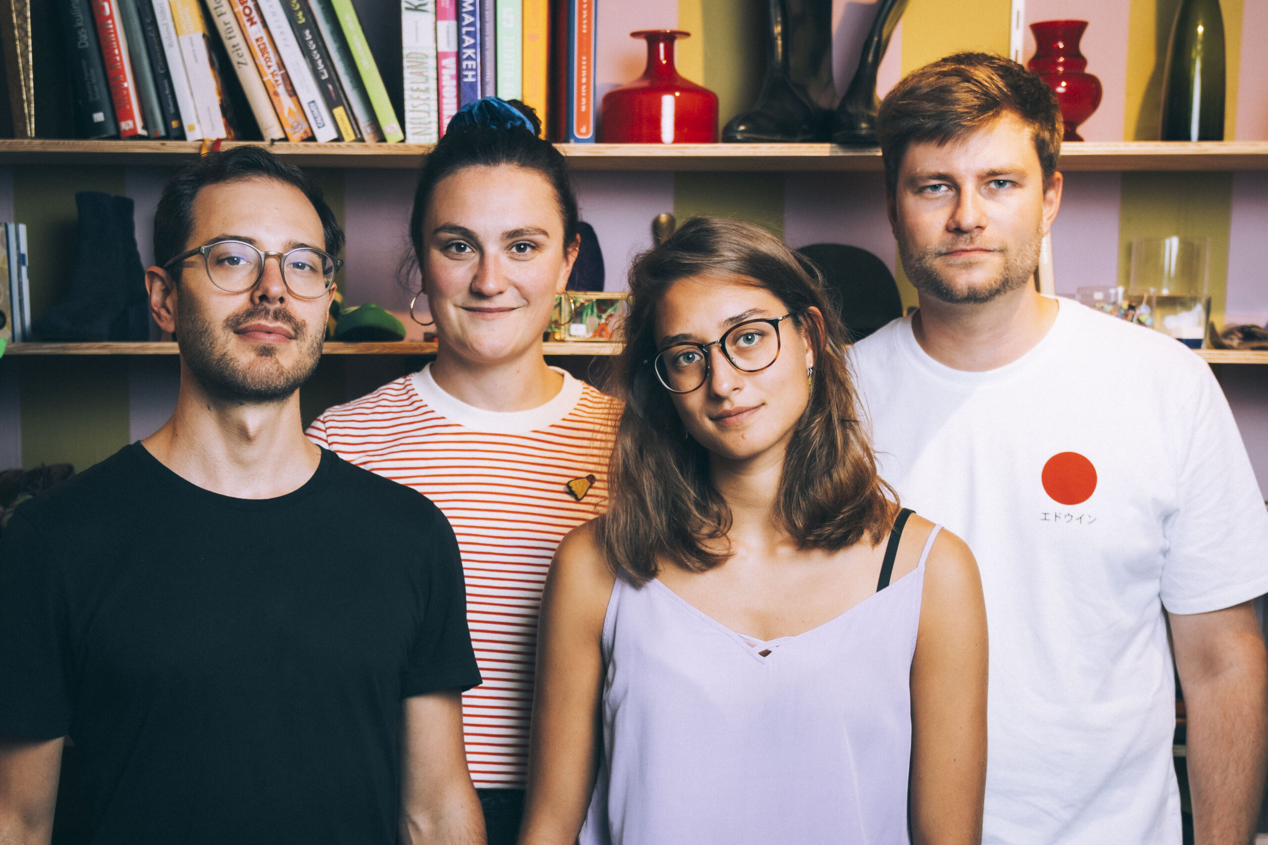 Simone-Felber_quartett_©Christian-Felber_DSC01731 Four friends posing for a group photo indoors in front of a colorful bookshelf.