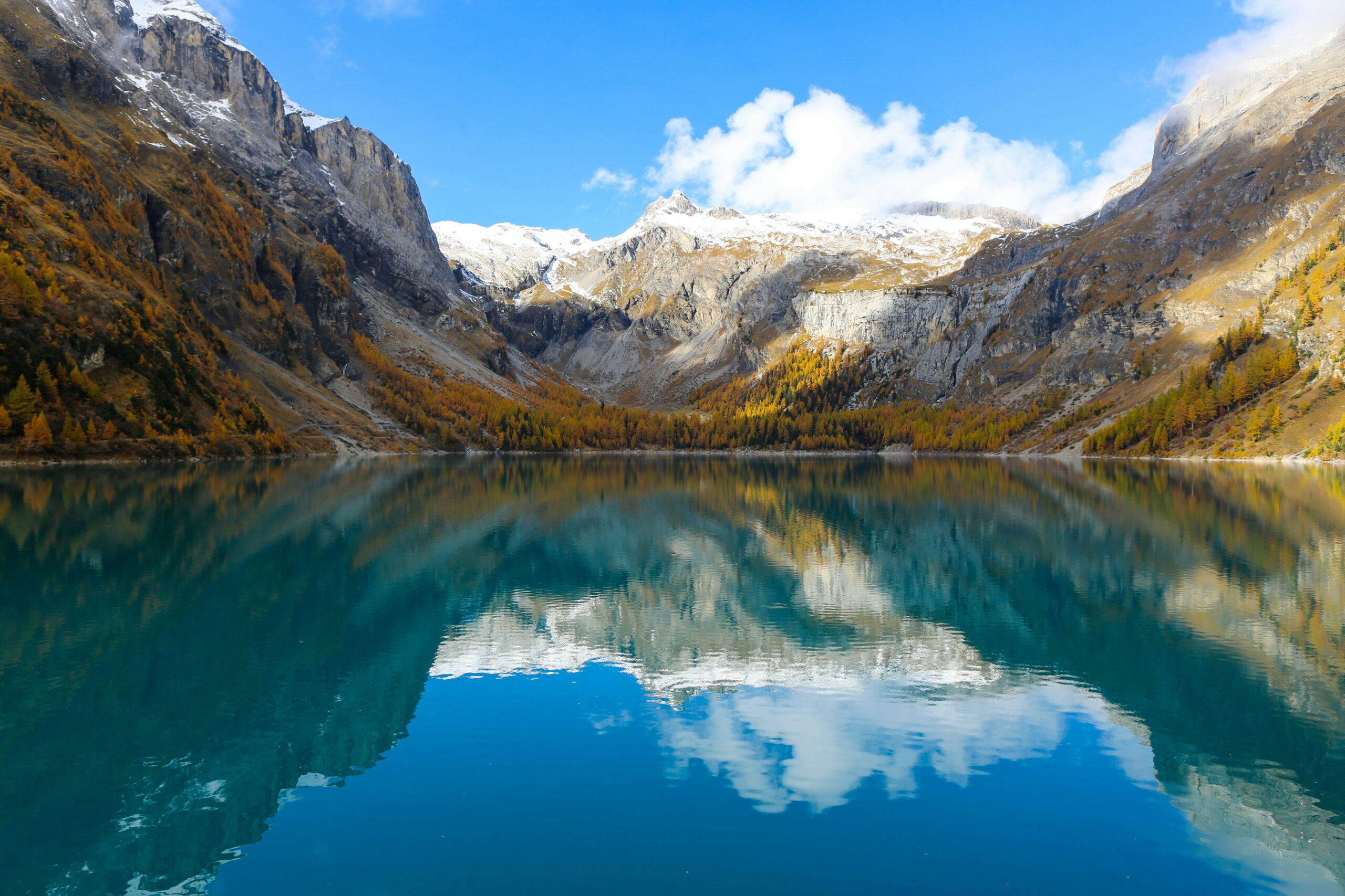 Snow-capped mountains reflect on a turquoise alpine lake beneath a clear blue sky.
